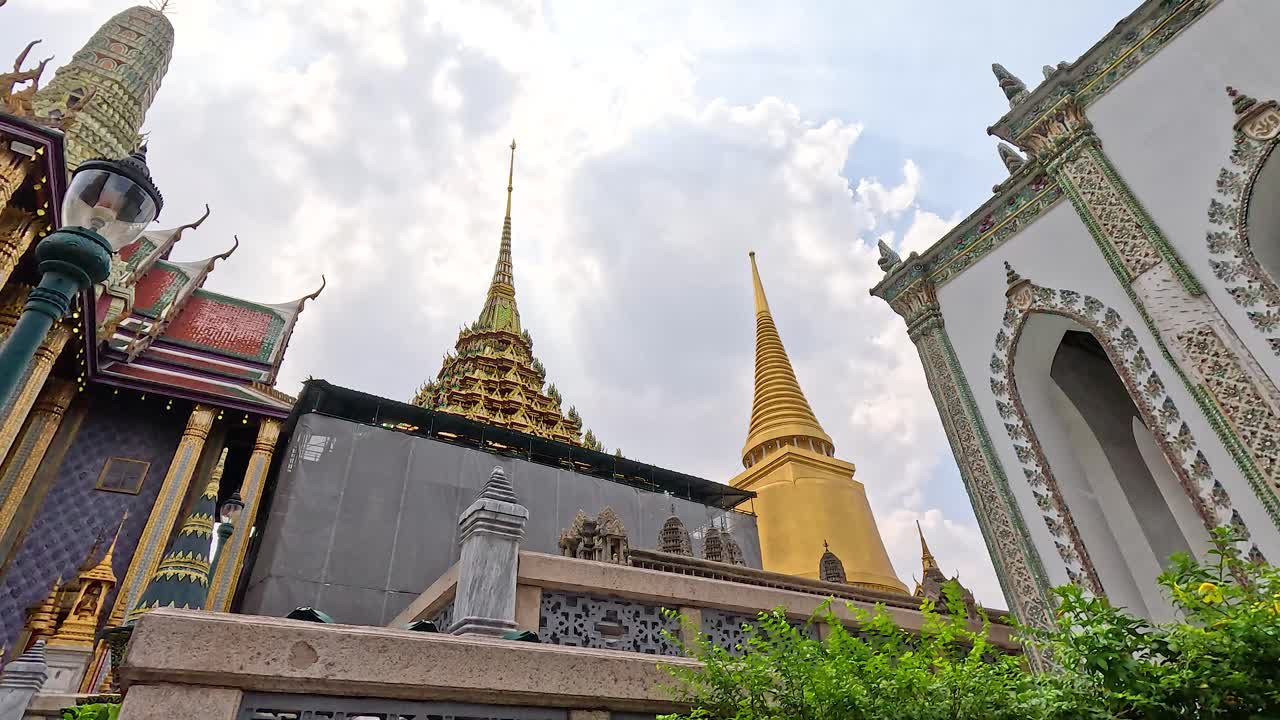 방의 wat phra kaew의 황금 첨탑의 역동적인 전망, 밝은 하늘 아래 복잡한 건축을 보여줍니다.