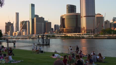 family and friends gather for a picnic on river quay green, south bank on the weekend, overlooking at brisbane river views and downtown cityscape at sunset, time-lapse shot.