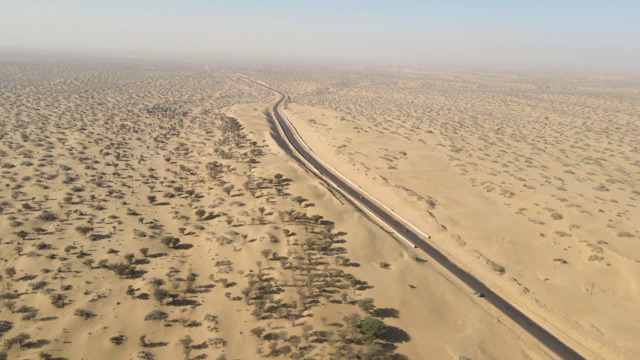 Aerial drone shot capturing a biker riding between sand dunes under the blazing sun in Rajasthan.
