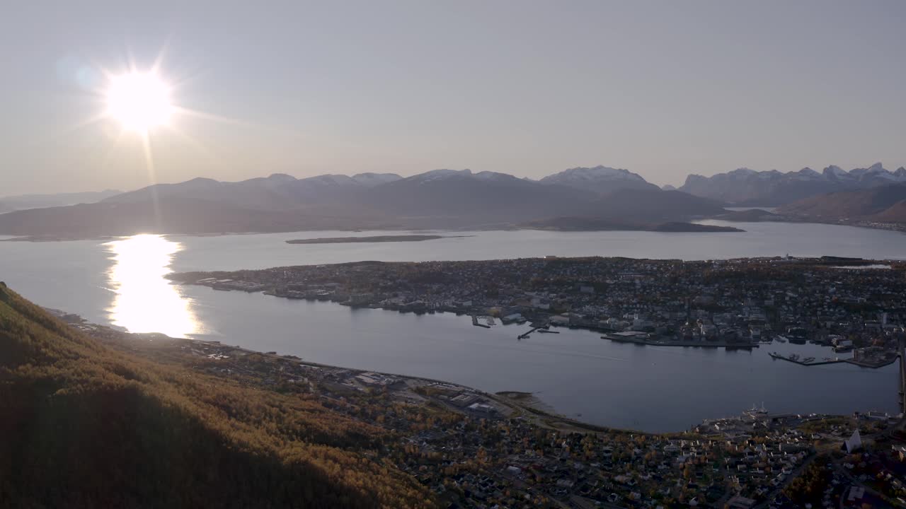 Aerial pan shot of Tromso with big sun in the sky seen from the mountain and viewpoint called fjellheisen