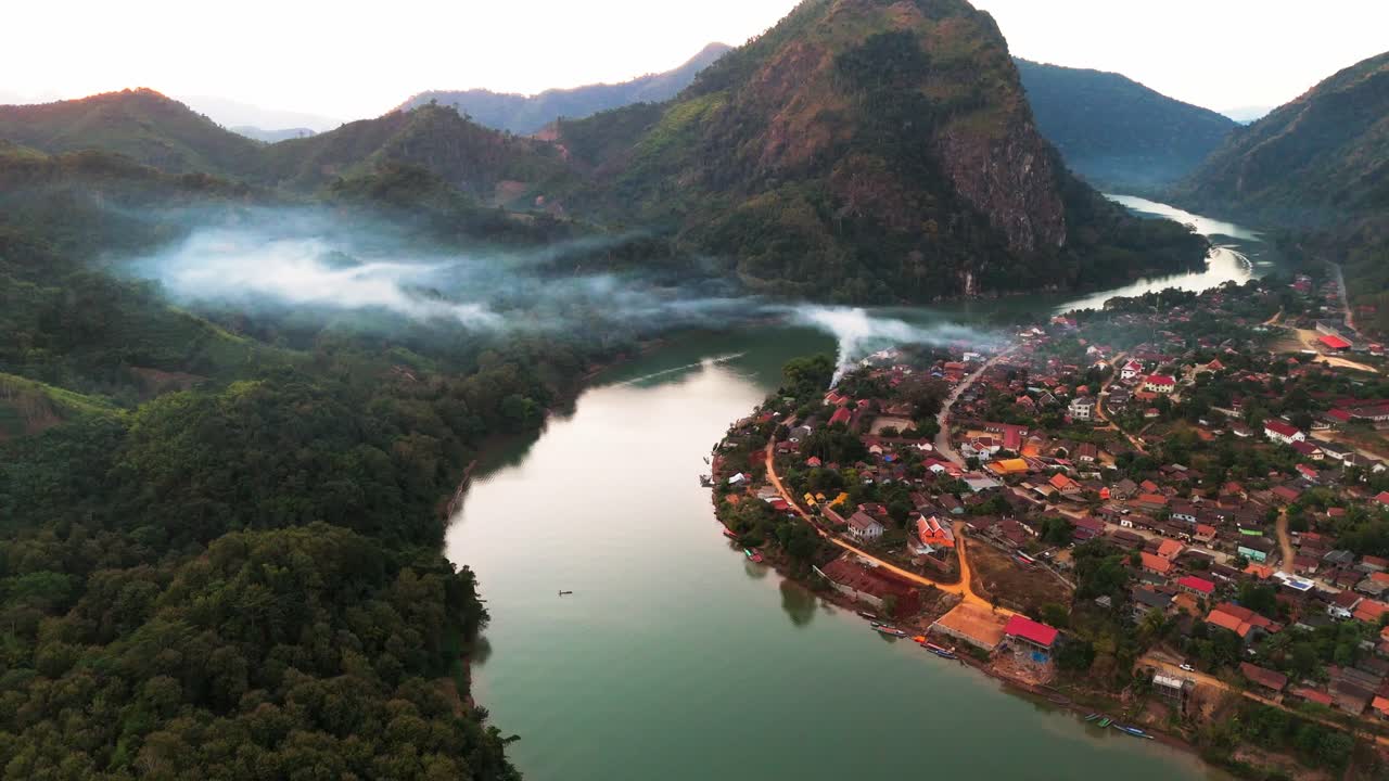 Aerial overview of Nong Khiaw, Laos, with flowing river and lush green hills in sunlight