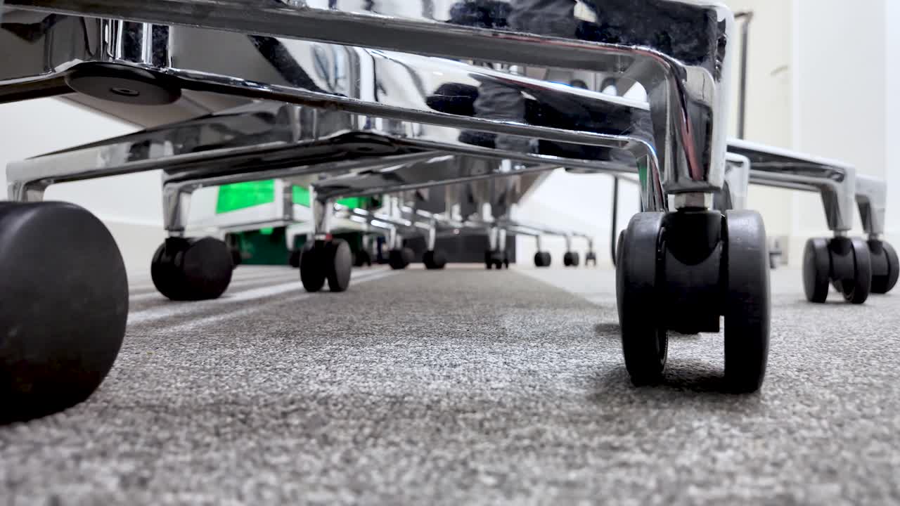 Caster wheels rolling underside office chairs on grey carpet with a low angle perspective
