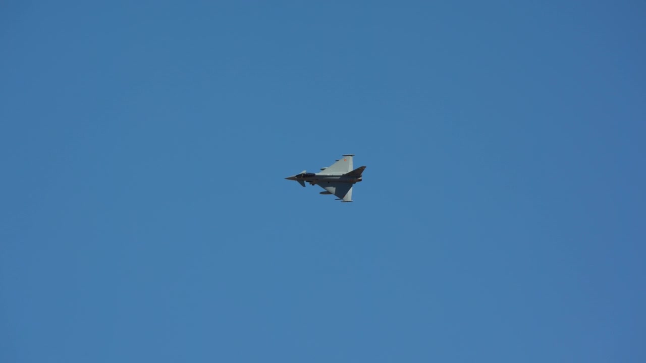 Military fighter jet flying across a clear blue sky, captured in slow motion during daytime flight