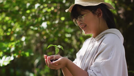 chica asiática sosteniendo una planta en el jardín en un día soleado sonriendo