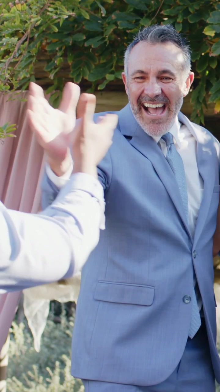 Vertical video: Laughing as hand reaching, man in suit exchanging high-fives at garden, celebrating