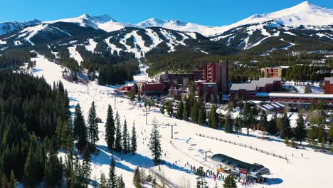 Chairlift-at-the-Bottom-of-Ski-Slope-in-Breckenridge,-Colorado-with-People-Skiing-and-Snowboarding-next-to-Hotels-and-Resort