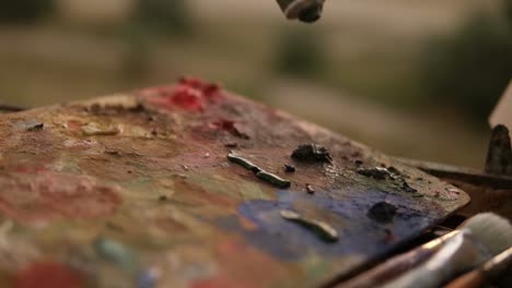 close up of a woman's hand artist squeezes out the paints from the tube on palette. preparing for art work outdoors