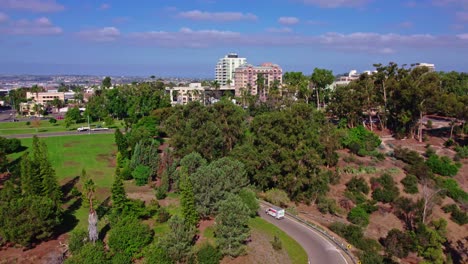 Seguimiento-De-La-Vista-Aérea-De-La-Conducción-De-Camiones-A-Lo-Largo-De-La-Carretera-De-La-Colina-En-El-área-Urbana-De-San-Diego-California,-Calles-Y-Edificios-Modernos-En-La-Parte-Superior-Del-Parque-De-La-Colina-Verde,-Paisaje-Urbano-Del-Centro-Con-Horizonte