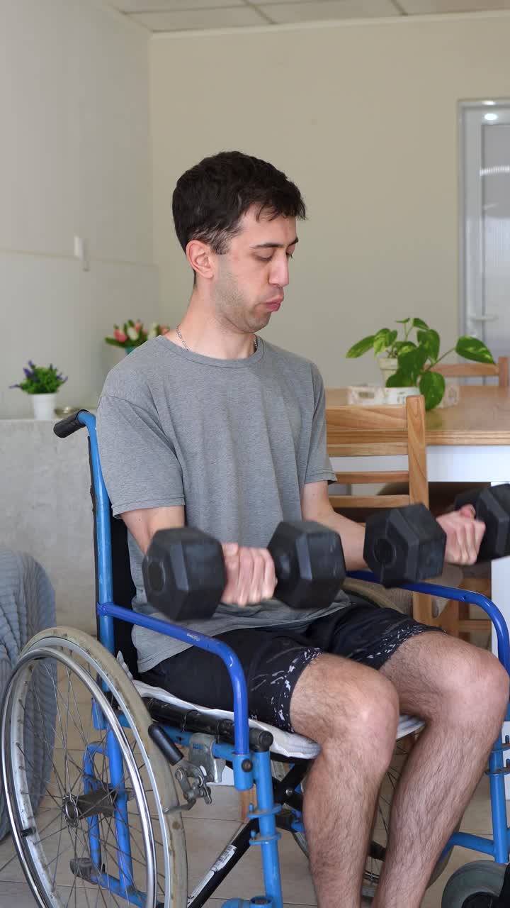 Young man in a wheelchair trains his biceps with dumbbells at home. Motivational fitness scene showing determination, strength, recovery and exercise for an active lifestyle, vertical format