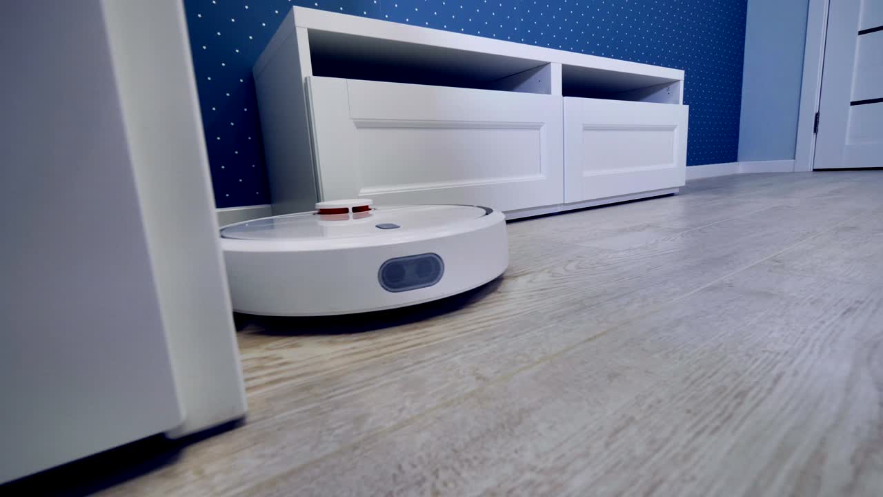 A robotic vacuum moves along several pieces of white furniture.