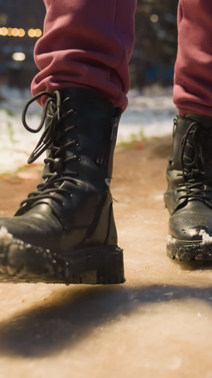 primer plano de la bota pisando un sendero cubierto de nieve en el parque de invierno. suelo nevado, clima frío, luces de la calle iluminadas creando una escena urbana de invierno en el parque de la ciudad