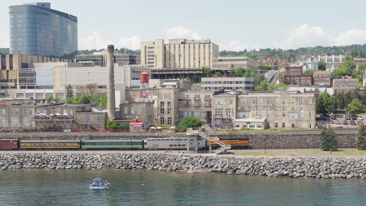 Veduta aerea dei binari ferroviari lungo il lungomare di Duluth, Minnesota, con edifici storici, lo skyline del centro e la costa rocciosa.
