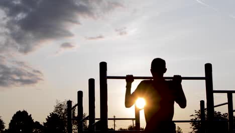 young male exercising on bar at sunrise