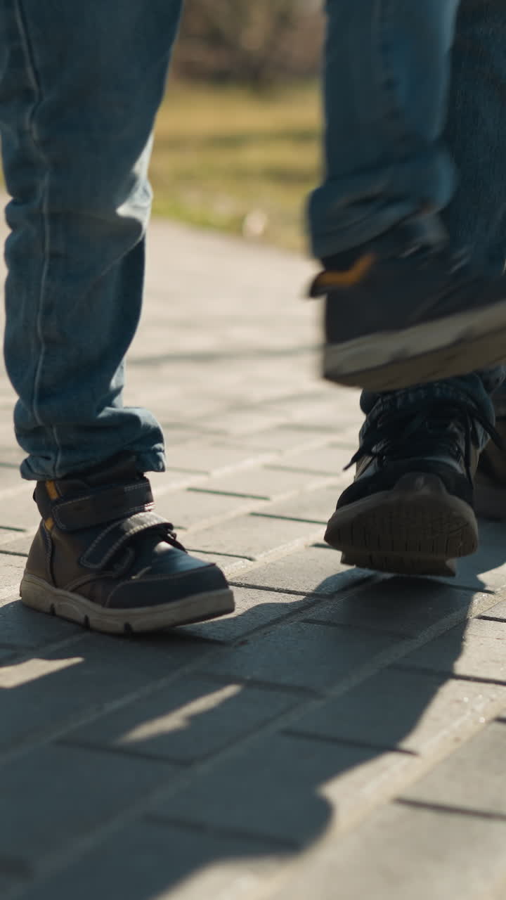 un primer plano de las piernas de dos personas, un adulto y un niño, mientras están jugando estampando allí las piernas en el pavimento juntos ambos llevan vaqueros azules y botas robustas
