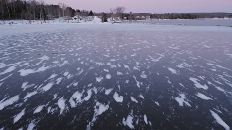 flying low towards shore above snowy patterns in dark ice at dawn aerial