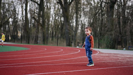 energetic caucasian kid runs by the stadium. active kid runs up to a ball to kick it. children play football at backdrop.