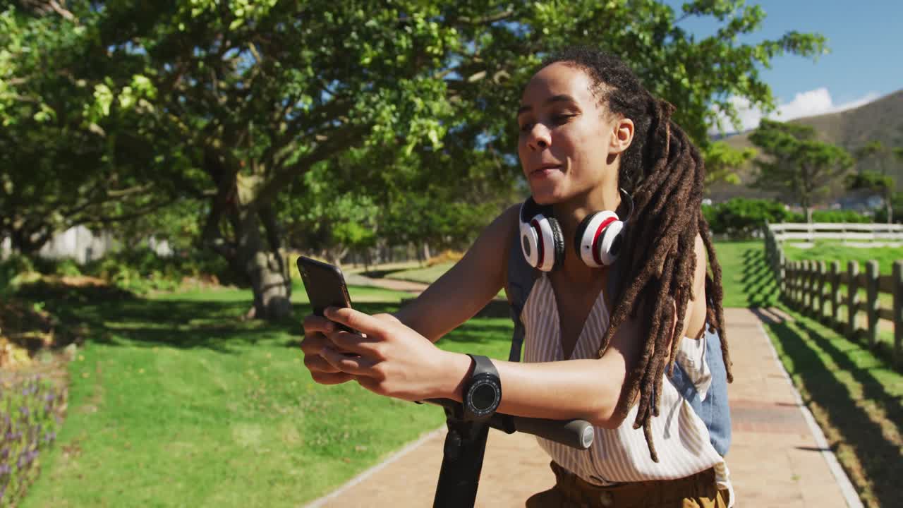 African american woman on scooter using smartphone and smiling