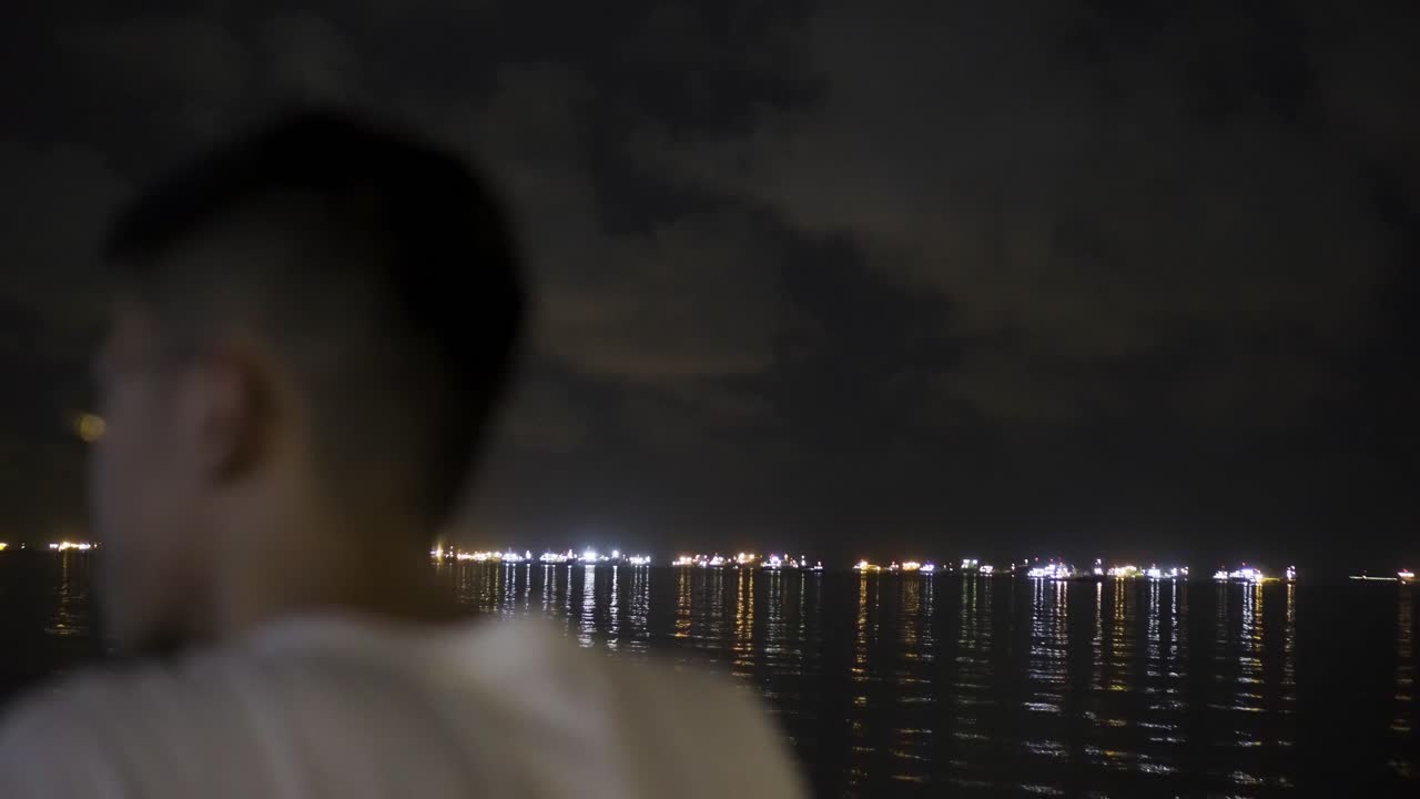 Man looking out towards the horizon with ship lights at night at East Coast Park, Singapore