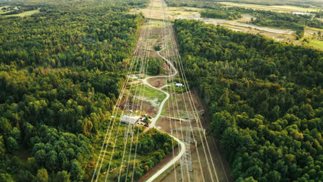 aerial flyover of high voltage transmission power lines passing through dense forest in rural countryside