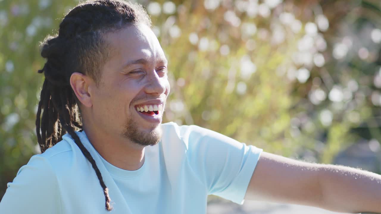 Adult African American man laughing tilting right sitting in garden showing white watch copy space