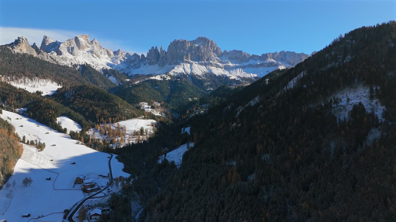 4K drone footage of the Rosengarten Catinaccio mountain range above the alpine valley near Tiers Tires in South Tyrol (Alto Adige), Italy, with snowy fields and forested slopes