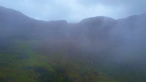 Vista-Aérea-De-Las-Montañas-Del-Parque-Nacional-Cajas-En-Cuenca-Ecuador-A-Través-De-Las-Nubes-Y-Con-Vista-A-Una-Cascada-Ubicada-En-Una-De-Las-Montañas-En-La-Parte-Más-Alta-Del-Parque