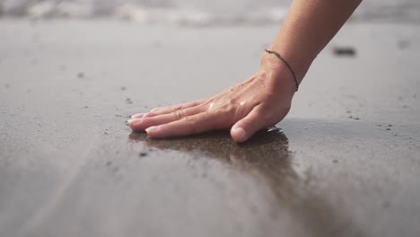 mano tocando la arena negra de la playa volcánica mientras se pone el sol en fuerteventura, islas canarias