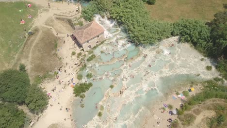 Vista-Aérea-De-Las-Famosas-Aguas-Termales-De-Saturnia-En-Toscana,-Italia,-Colinas-De-Maremma,-Paisaje-Escénico,-Gente-Reunida-En-Una-Piscina-Natural.