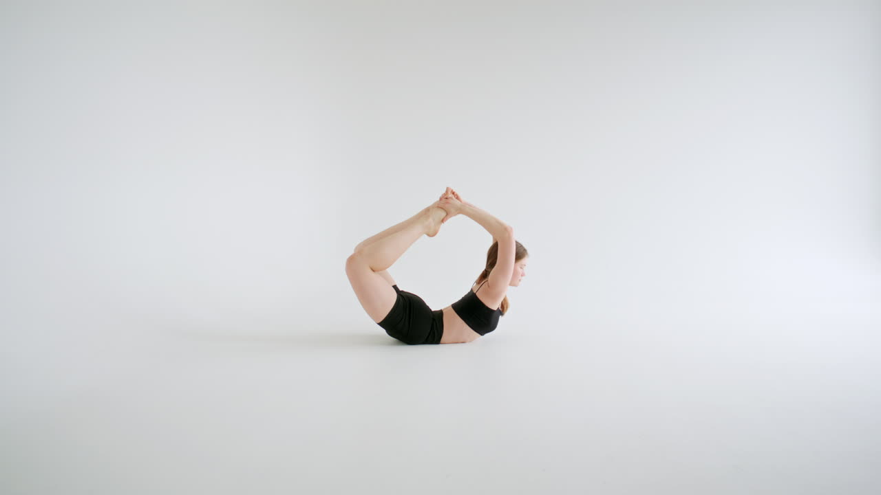 Junge Frau macht die Bogen-Yoga-Pose vor einem weißen Hintergrund