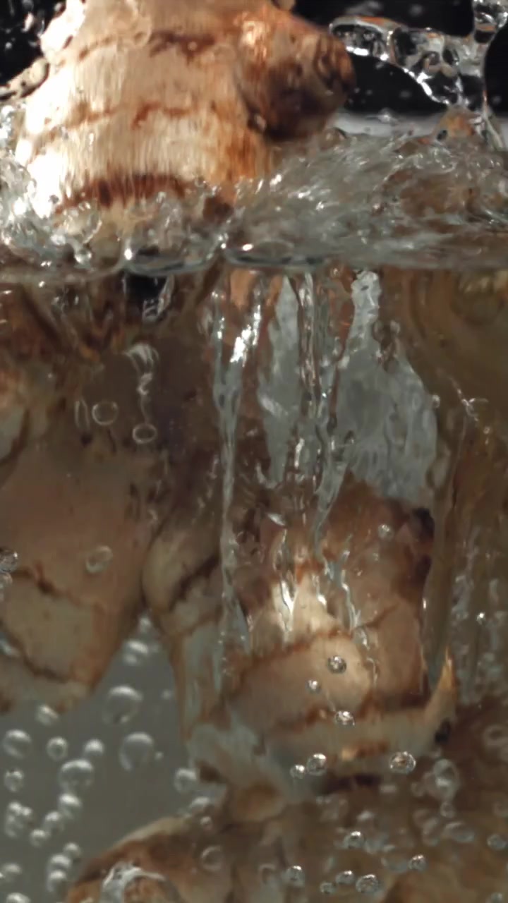 Radici di zenzero fresche che schizzano nell'acqua limpida al rallentatore