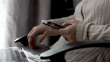 close up of female hand, scrolling on mobile with laptop on lap