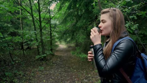 A young girl with long hair is enjoying a cup of hot drink on the road in the forest