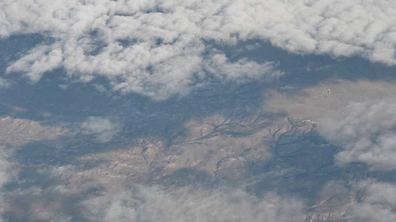 Aerial drone footage above layered clouds revealing vast mountain ridges and arid terrain below