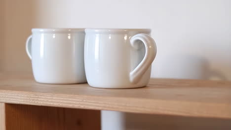 two white ceramic mugs on a wooden shelf