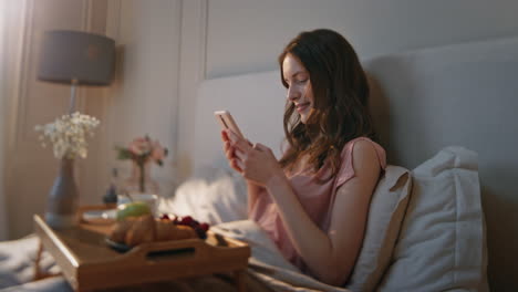 pretty girl looking cell in morning bed. relaxed attractive model holding cup