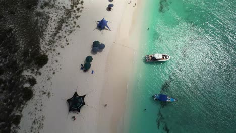 Playa-De-Los-Roques-En-Venezuela-Con-Coloridas-Sombrillas-Y-Un-Barco-En-Aguas-Cristalinas-De-Color-Turquesa,-Vista-Aérea