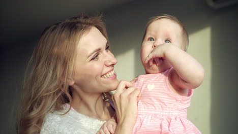 happy mother holding baby girl on hands. cheerful mom embrace toddler girl