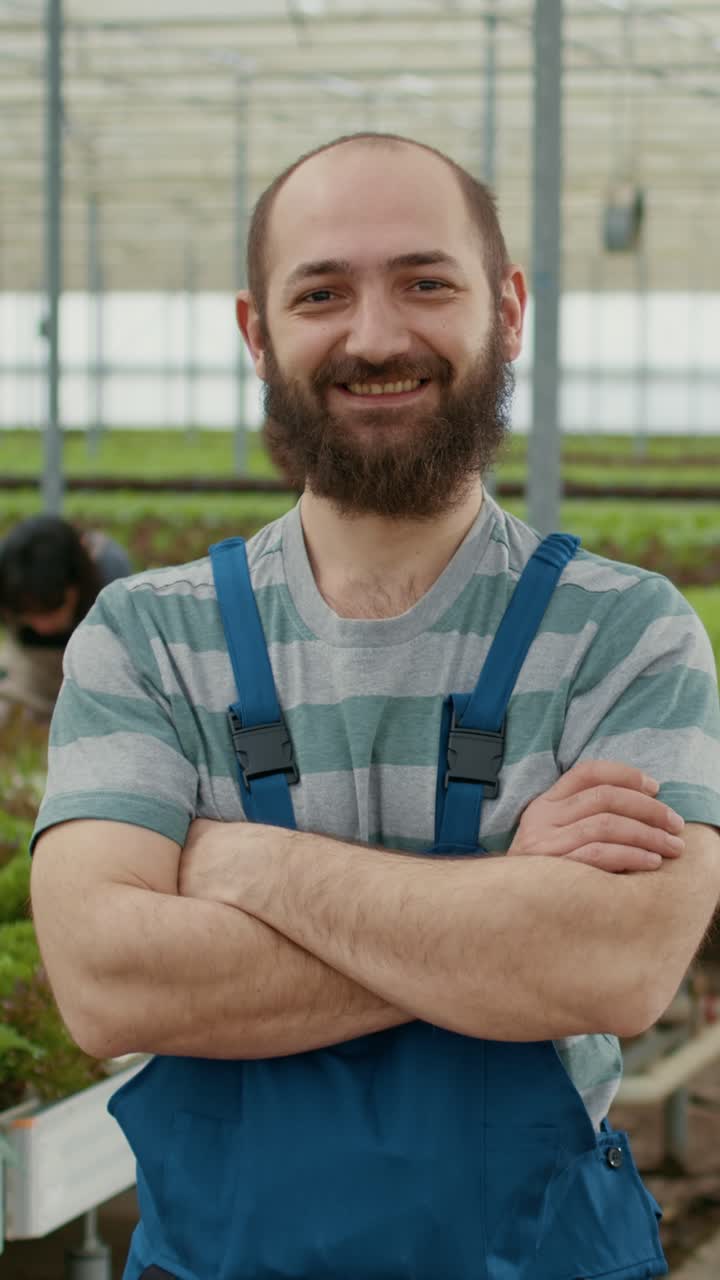 Ritratto di un agricoltore caucasico in una fattoria di alimenti biologici, in posa sicura mentre i raccoglitori raccolgono le verdure