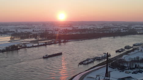 aerial of cargo ship on river with a setting sun in the background in winter - close