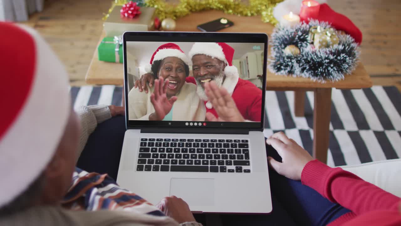 madre y hija afroamericanas usando una computadora portátil para una videollamada de navidad con la pareja en la pantalla