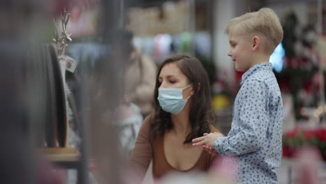 mother and daughter go shopping and choose christmas trees and toys with decorations for christmas in protective masks