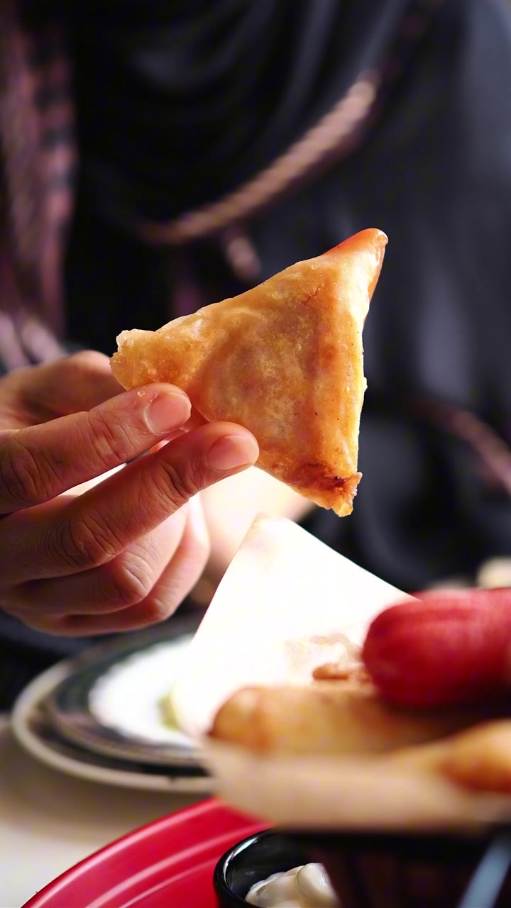 Primo piano di una mano che tiene un samosa dorato