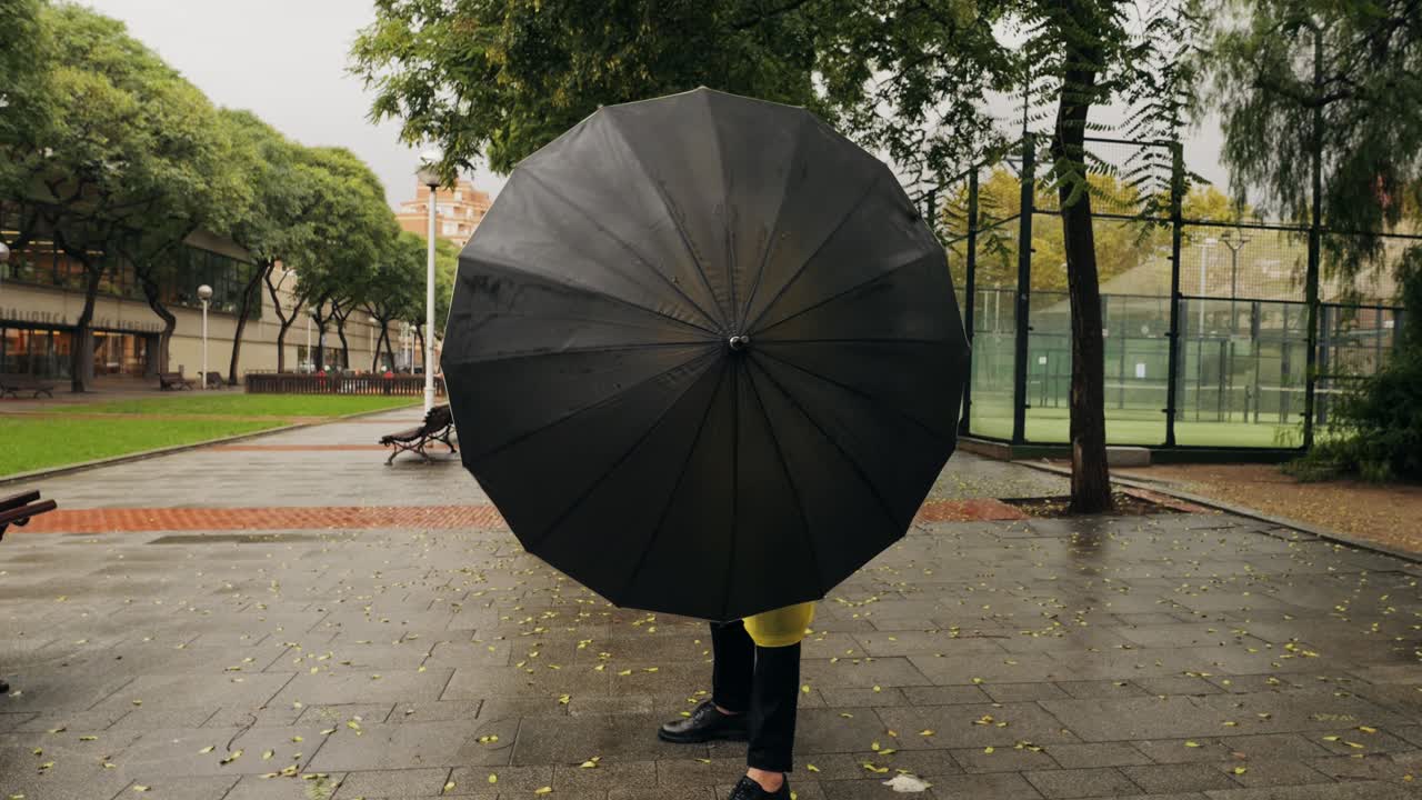 Business man tourist person with umbrella and raincoat on rainy european city street, lights reflecting, walking in Barcelona or Amsterdam during the rain