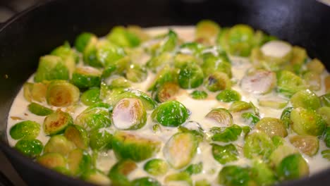 cooking roasted sautéed brussels sprouts in a cast iron pan skillet - pouring cream - close up macro shot