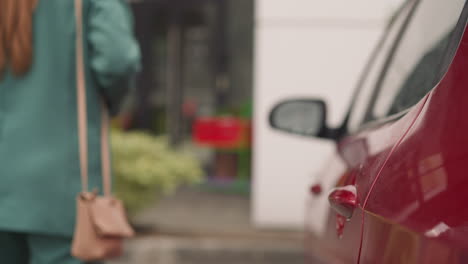 mujer elegante con bolsa de cuero cierra la puerta de un automóvil rojo