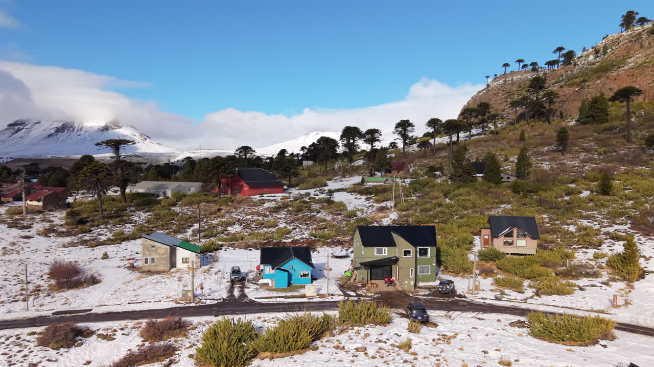 Aerial establishing fly Patagonian village of Caviahue, Traditional houses around Snowy mountain landscape with Araucaria trees