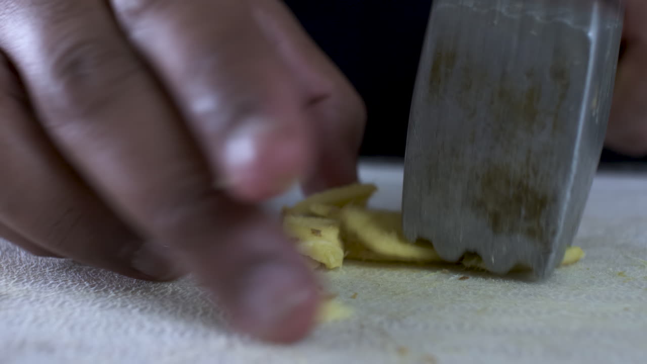 Hand Of Ethnic Minority Adult Male Using Tenderizer To Crush Fresh Cut Ginger On Cutting Board