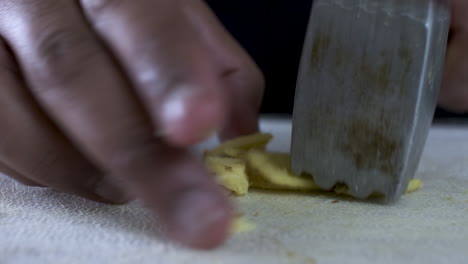 mano de un hombre adulto de una minoría étnica que usa un ablandador para aplastar el jengibre recién cortado en la tabla de cortar