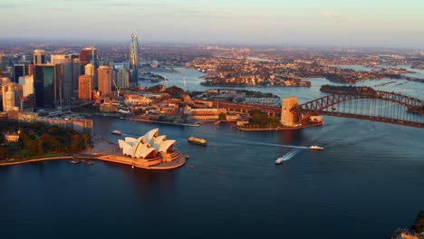 zoom out aerial view of sydney harbour bridge and opera house with ferry boats cruising at sunset