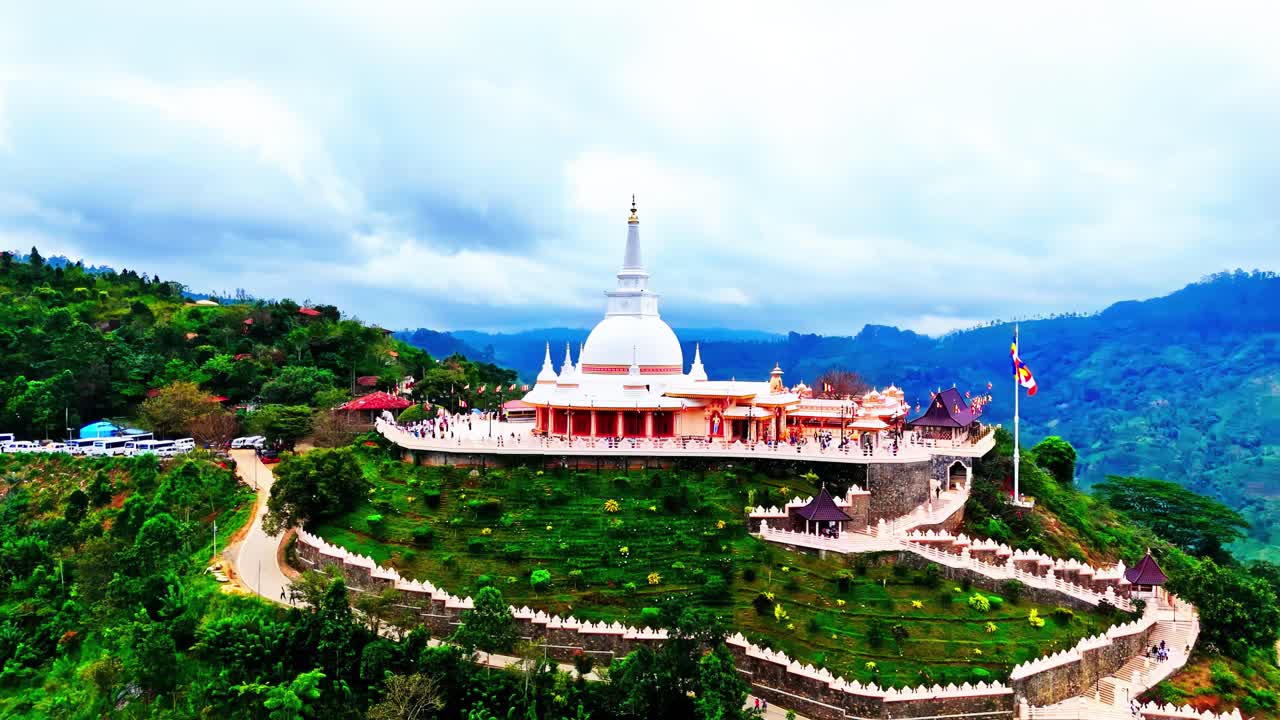A majestic Buddhist Asapuwa Temple crowns a Sri Lankan hilltop, featuring a gleaming white stupa, colorful flags, winding pathways, and panoramic views over vibrant green tropical hills.